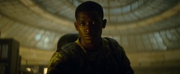 Movie still from “Outside the Wire” (2021), directed by Mikael Håfström – A man in camouflage sitting in a chair in the dark; Close Up shot, Low angle