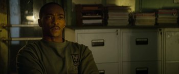 Movie still from “Outside the Wire” (2021), directed by Mikael Håfström – A man in a green shirt sitting in front of a filing cabinet; Close Up shot, Over the shoulder angle