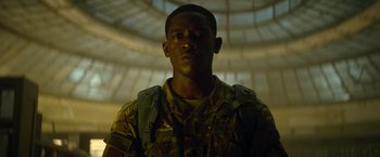 Movie still from “Outside the Wire” (2021), directed by Mikael Håfström – A man in a camouflage uniform stands in front of a building; Close Up shot, Low angle
