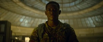 Movie still from “Outside the Wire” (2021), directed by Mikael Håfström – A man in a camouflage uniform standing in front of a building; Close Up shot, Low angle