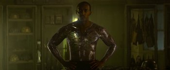 Movie still from “Outside the Wire” (2021), directed by Mikael Håfström – A man in a metallic body suit standing with his hands on his hips; Medium shot, Low angle