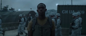 Movie still from “Outside the Wire” (2021), directed by Mikael Håfström – A man in a military uniform standing in front of a group of soldiers; Medium shot, Over the shoulder angle