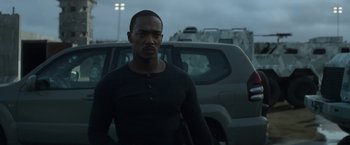 Movie still from “Outside the Wire” (2021), directed by Mikael Håfström – A man standing in front of a car in a parking lot; Medium shot, Over the shoulder angle