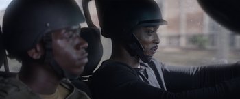 Movie still from “Outside the Wire” (2021), directed by Mikael Håfström – A man wearing a helmet while sitting in a car; Close Up shot, Over the shoulder angle
