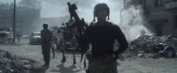 Movie still from “Outside the Wire” (2021), directed by Mikael Håfström – A man holding a gun while standing next to a group of soldiers; Medium shot, Low angle