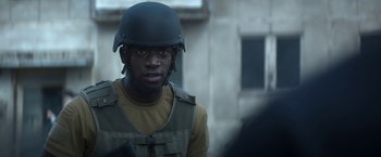 Movie still from “Outside the Wire” (2021), directed by Mikael Håfström – A man wearing a helmet is standing in front of a building; Close Up shot, Over the shoulder angle