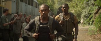 Movie still from “Outside the Wire” (2021), directed by Mikael Håfström – Two men are walking down the street with backpacks on; Medium shot, Low angle