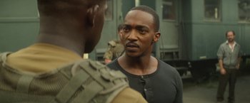 Movie still from “Outside the Wire” (2021), directed by Mikael Håfström – A man in a black shirt is talking to another man in fatigues; Close Up shot, Over the shoulder angle