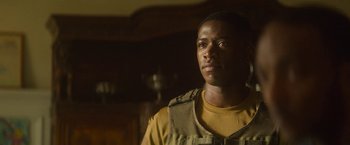 Movie still from “Outside the Wire” (2021), directed by Mikael Håfström – A man in a tan shirt is standing in a dark room; Close Up shot, Over the shoulder angle