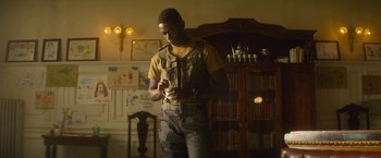 Movie still from “Outside the Wire” (2021), directed by Mikael Håfström – A man standing next to a bookshelf in a living room; Medium shot, Low angle