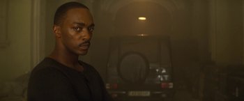 Movie still from “Outside the Wire” (2021), directed by Mikael Håfström – A man standing in front of a car in a dimly - lit room; Close Up shot, Over the shoulder angle
