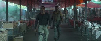 Movie still from “Outside the Wire” (2021), directed by Mikael Håfström – A couple of men walking down a street holding guns; Medium shot, Low angle