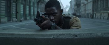 Movie still from “Outside the Wire” (2021), directed by Mikael Håfström – A man holding a gun while standing next to a wall; Close Up shot, Low angle