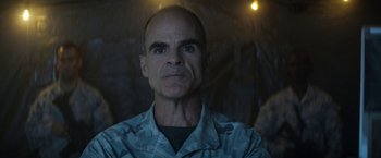 Movie still from “Outside the Wire” (2021), directed by Mikael Håfström – A man with a bald head wearing a camouflage shirt; Close Up shot, Low angle