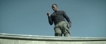 Movie still from “Outside the Wire” (2021), directed by Mikael Håfström – A man standing on top of a cement ledge; Medium shot, Low angle