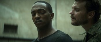 Movie still from “Outside the Wire” (2021), directed by Mikael Håfström – A man standing next to another man with his eyes closed; Close Up shot, Over the shoulder angle