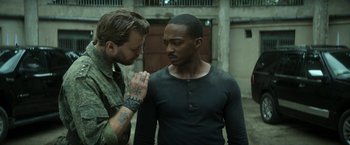 Movie still from “Outside the Wire” (2021), directed by Mikael Håfström – Two men standing next to each other in front of a building; Medium shot, Over the shoulder angle