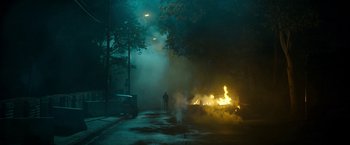 Movie still from “Outside the Wire” (2021), directed by Mikael Håfström – A person standing in front of a fire on a street; Extreme Wide shot, High angle