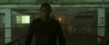 Movie still from “Outside the Wire” (2021), directed by Mikael Håfström – A man standing in a dark room looking at the camera; Medium shot, Low angle