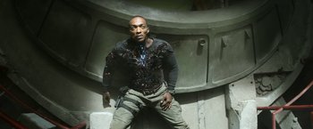 Movie still from “Outside the Wire” (2021), directed by Mikael Håfström – A man with a gun sitting on the ground in front of a wall; Medium shot, Overhead angle