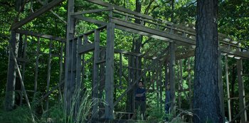 Movie still from “Ozark” (2017), created by Bill Dubuque – A man standing in front of a wooden structure in the woods; Extreme Wide shot, Low angle
