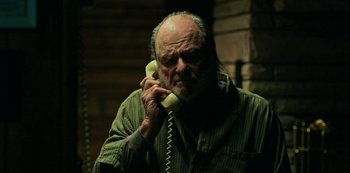 Movie still from “Ozark” (2017), created by Bill Dubuque – An older man talking on a phone while standing in front of a brick wall; Medium shot, Low angle