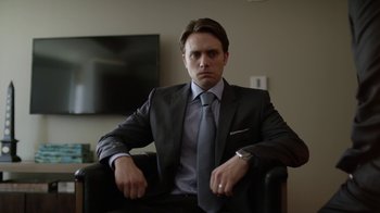 Movie still from “Mr. Robot” (2015), created by Sam Esmail – A man in a suit and tie sitting in a chair; Medium shot, Over the shoulder angle