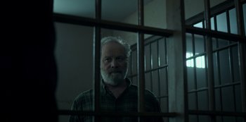 Movie still from “Ozark” (2017), created by Bill Dubuque – An older man standing behind bars in a jail cell; Medium shot, Low angle