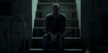 Movie still from “Ozark” (2017), created by Bill Dubuque – A man sitting on the stairs holding a remote control; Medium shot, Low angle