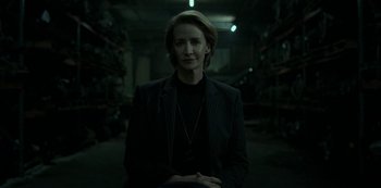 Movie still from “Ozark” (2017), created by Bill Dubuque – A woman standing in a dark room in front of shelves; Medium shot, Low angle
