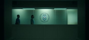 Movie still from “Ozark” (2017), created by Bill Dubuque – A person standing in front of a wall with a police badge on it; Wide shot, Low angle