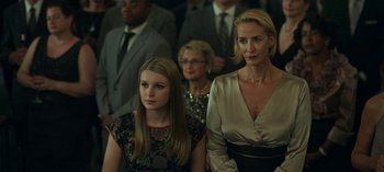 Movie still from “Ozark” (2017), created by Bill Dubuque – Two women and a man are sitting in front of other people; Close Up shot, Over the shoulder angle