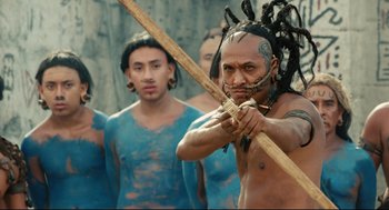 Movie still from “Apocalypto” (2006), directed by Mel Gibson – A man holding a bow and arrow in front of a group of people; Medium shot, Over the shoulder angle