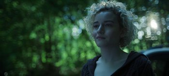 Movie still from “Ozark” (2017), created by Bill Dubuque – A woman with curly blonde hair standing in front of trees; Close Up shot, Low angle