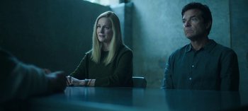 Movie still from “Ozark” (2017), created by Bill Dubuque – A woman sitting at a table in front of a wall; Medium shot, High angle