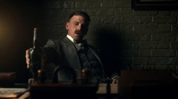 Movie still from “Peaky Blinders” (2013), created by Steven Knight – A man in a suit sitting in front of a brick wall; Medium shot, Low angle