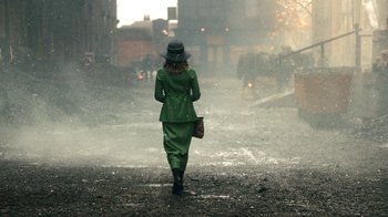 Movie still from “Peaky Blinders” (2013), created by Steven Knight – A woman in a green suit walking down a street; Wide shot, Over the shoulder angle