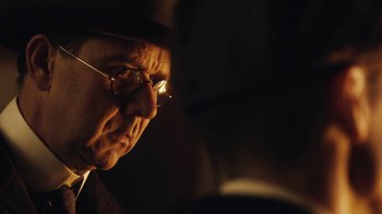 Movie still from “Peaky Blinders” (2013), created by Steven Knight – An older man wearing glasses and a hat; Close Up shot, Over the shoulder angle