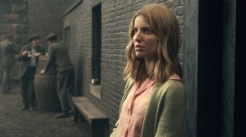 Movie still from “Peaky Blinders” (2013), created by Steven Knight – A woman standing in front of a brick wall; Medium shot, Over the shoulder angle