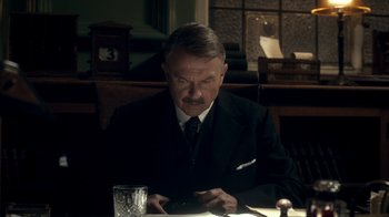Movie still from “Peaky Blinders” (2013), created by Steven Knight – An older man sitting at a table looking at his cell phone; Close Up shot, Low angle