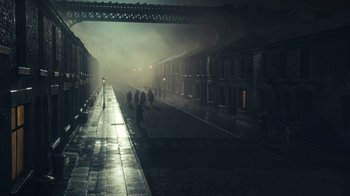Movie still from “Peaky Blinders” (2013), created by Steven Knight – People are walking down a street in the dark; Extreme Wide shot, High angle