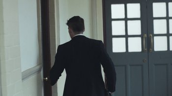 Movie still from “Peaky Blinders” (2013), created by Steven Knight – A man in a suit is walking through a door way; Medium shot, Over the shoulder angle