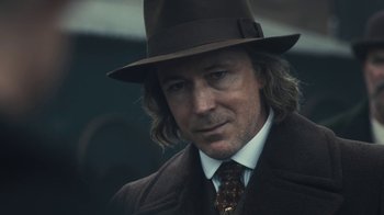 Movie still from “Peaky Blinders” (2013), created by Steven Knight – A person wearing a suit and hat; Close Up shot, Over the shoulder angle