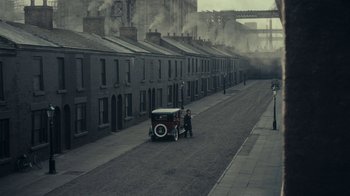 Movie still from “Peaky Blinders” (2013), created by Steven Knight – An old car is parked on the side of the street; Extreme Wide shot, High angle