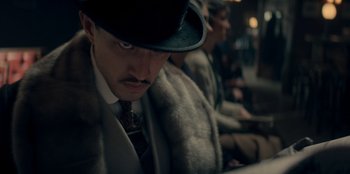 Movie still from “Peaky Blinders” (2013), created by Steven Knight – A person wearing a hat on a train; Close Up shot, Low angle