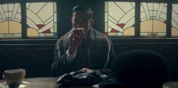 Movie still from “Peaky Blinders” (2013), created by Steven Knight – A man sitting in front of a window eating a sandwich; Medium shot, Over the shoulder angle