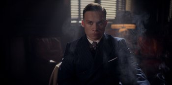 Movie still from “Peaky Blinders” (2013), created by Steven Knight – A man in a suit and tie sitting in front of a window; Medium shot, Low angle