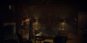 Movie still from “Peaky Blinders” (2013), created by Steven Knight – A man standing in front of a couch in a living room; Wide shot, Low angle