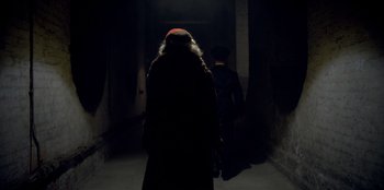 Movie still from “Peaky Blinders” (2013), created by Steven Knight – A man in a long brown coat and a man in a red hat; Medium shot, Low angle