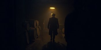 Movie still from “Peaky Blinders” (2013), created by Steven Knight – A man walking in a dark room in a warehouse; Wide shot, Low angle
